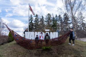 Cilvēki stāv kalnā pie koka baltiem burtiem Vandāni. Aizmugurē Sēlijas karogs.