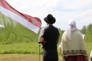 Vīrietis un sieviete tautastērpos ar pagrieztru muguru stāv pie Sēlijas karoga.